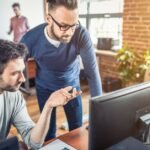 Two coworkers reviewing a website design on desktop monitors in a modern office