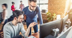 Two coworkers reviewing a website design on desktop monitors in a modern office