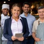How to Register a Business in Ontario: Key Steps & Requirements Group of small business owners and staff standing together in a restaurant, with a woman in business attire holding a tablet at the center
